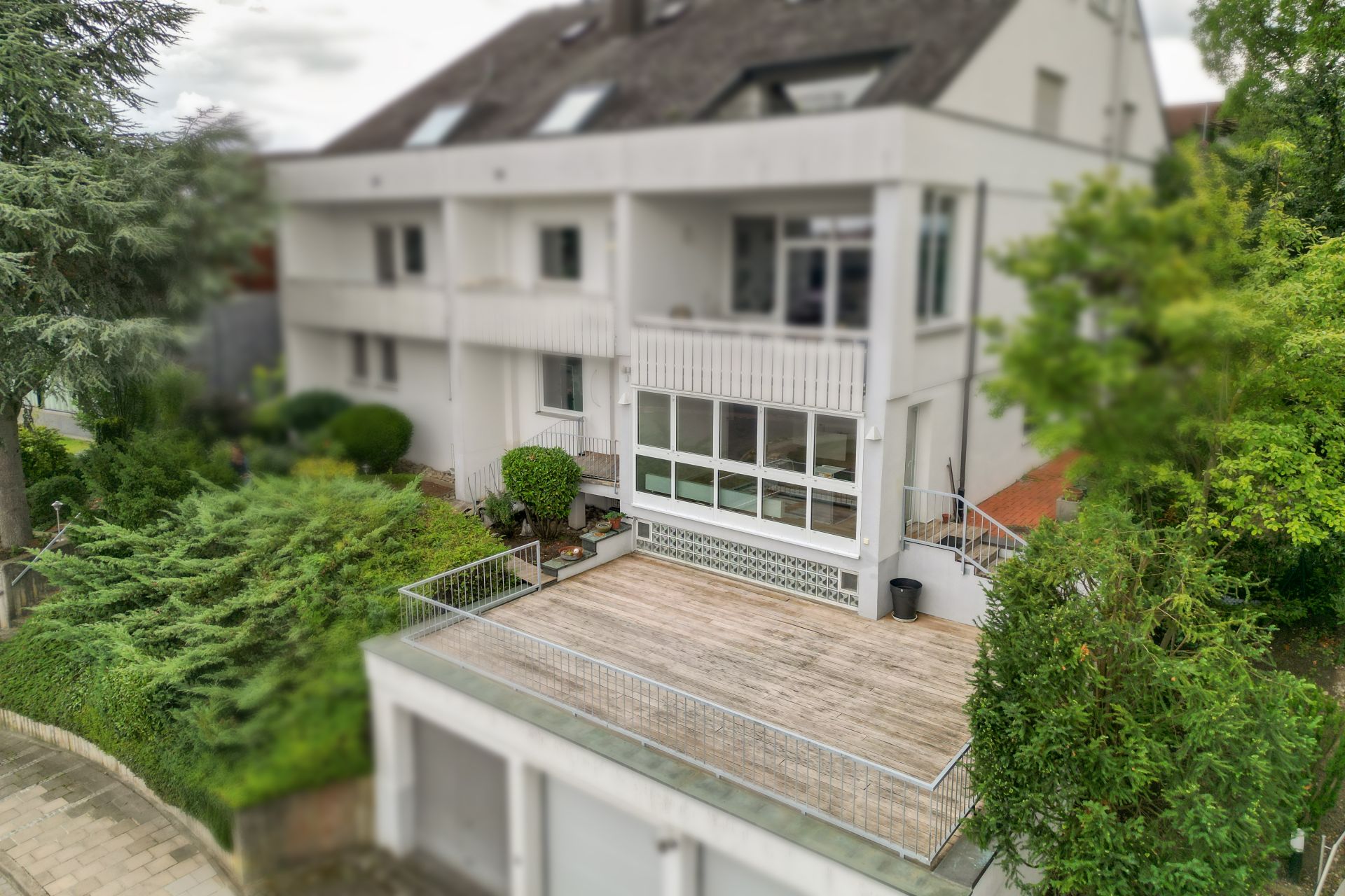 Mehrfamilienhaus mit großem Balkon und Garten, umgeben von Bäumen und Sträuchern.