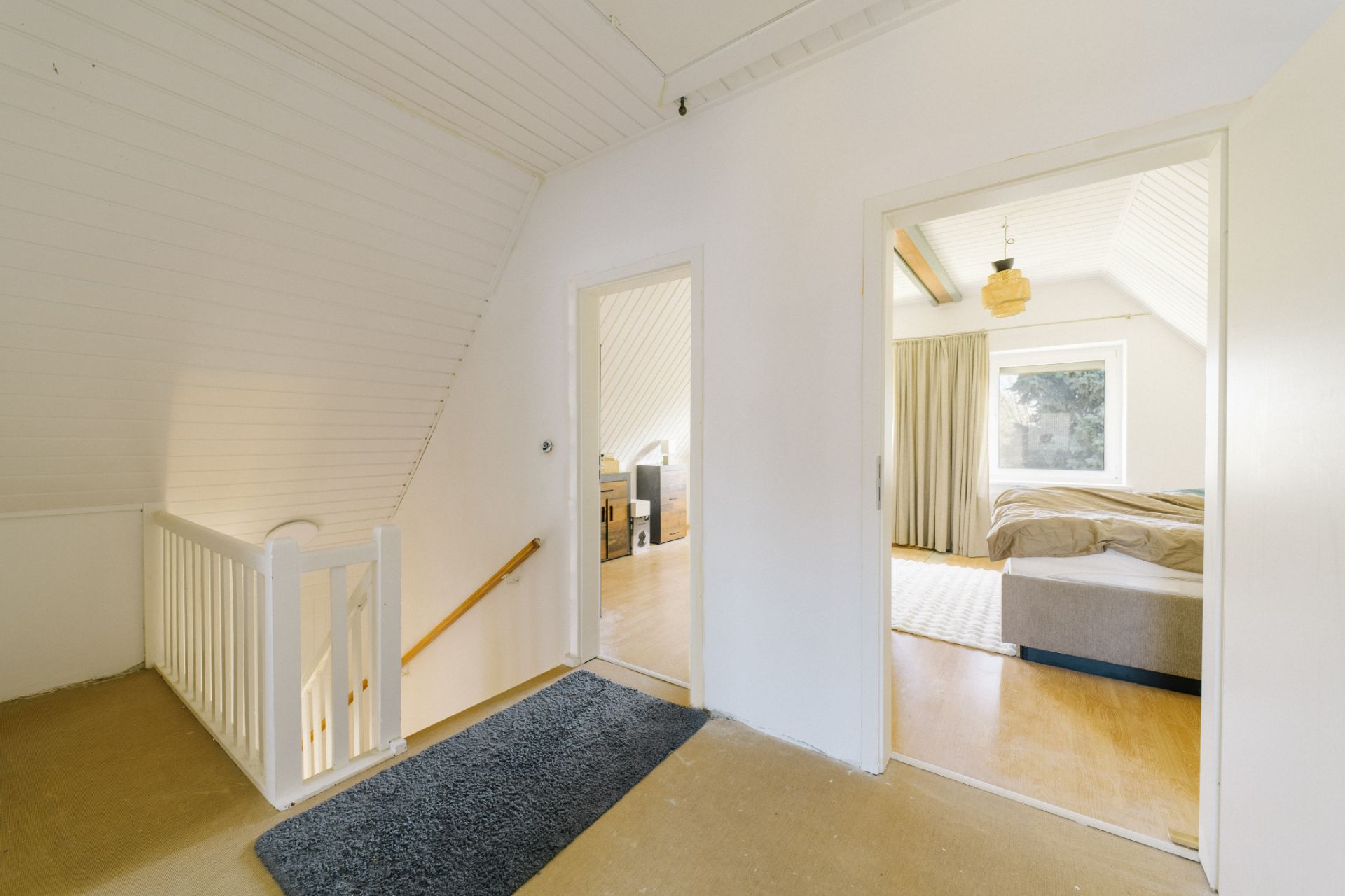 Heller Flur mit Teppich und Zugang zu zwei Schlafzimmern, Treppe links.