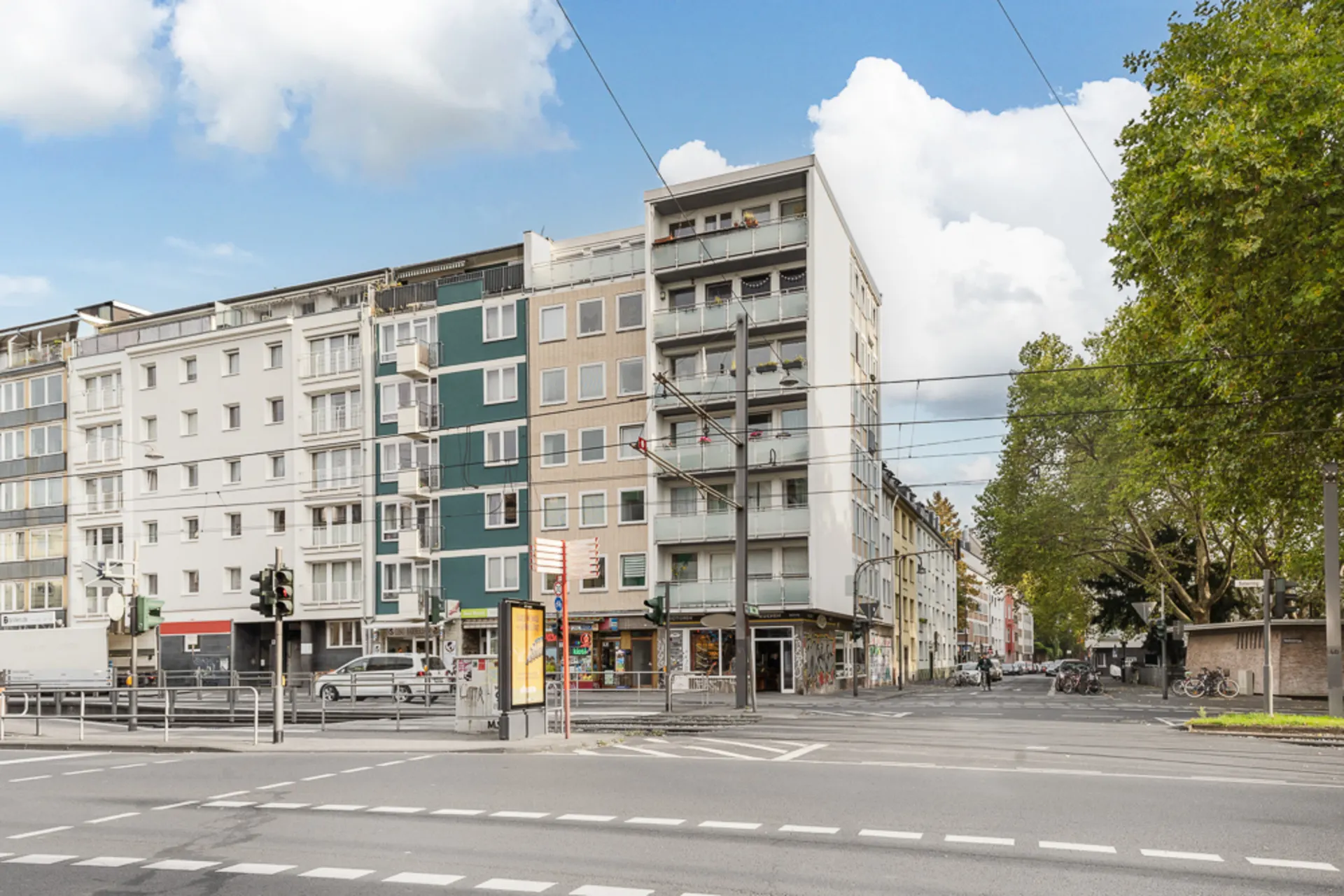 Mehrstöckiges Wohnhaus an einer Straßenecke mit Balkonen und Geschäften im Erdgeschoss.