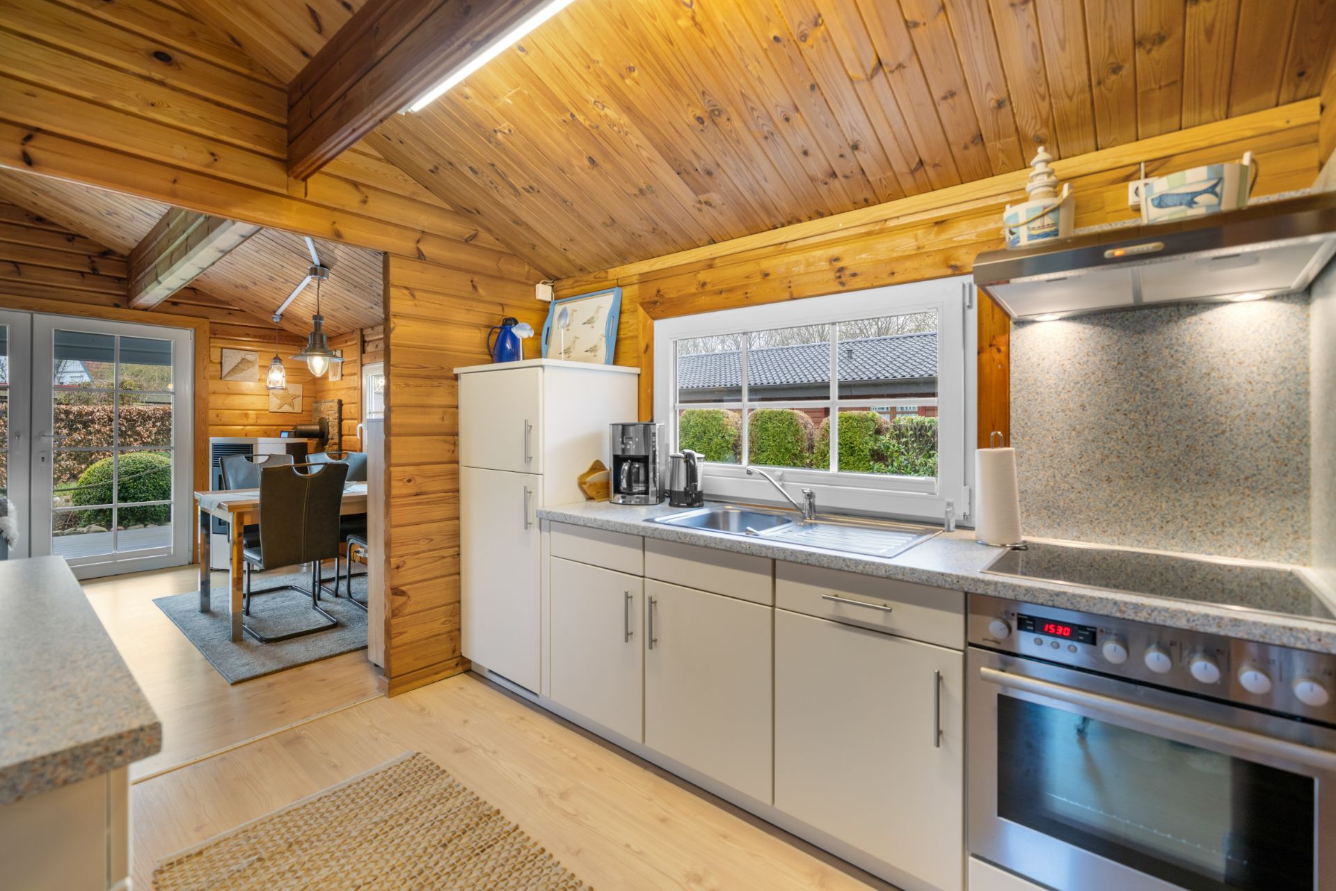 Helle Holzküche mit weißen Schränken, Herd, Spüle, Fenster und Blick ins Esszimmer.