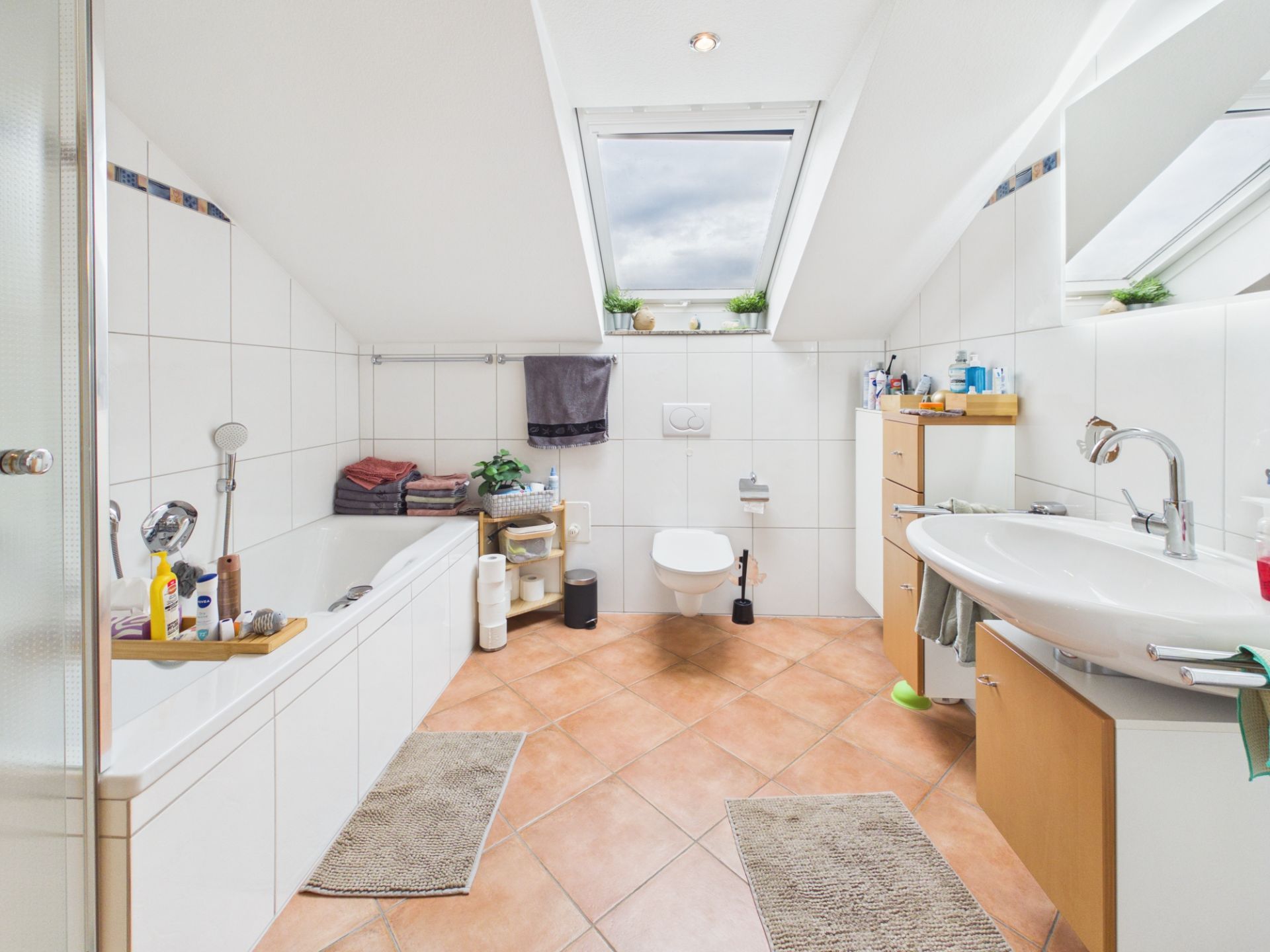 Helles Badezimmer mit Badewanne, WC, Waschbecken und zwei Dachfenstern.