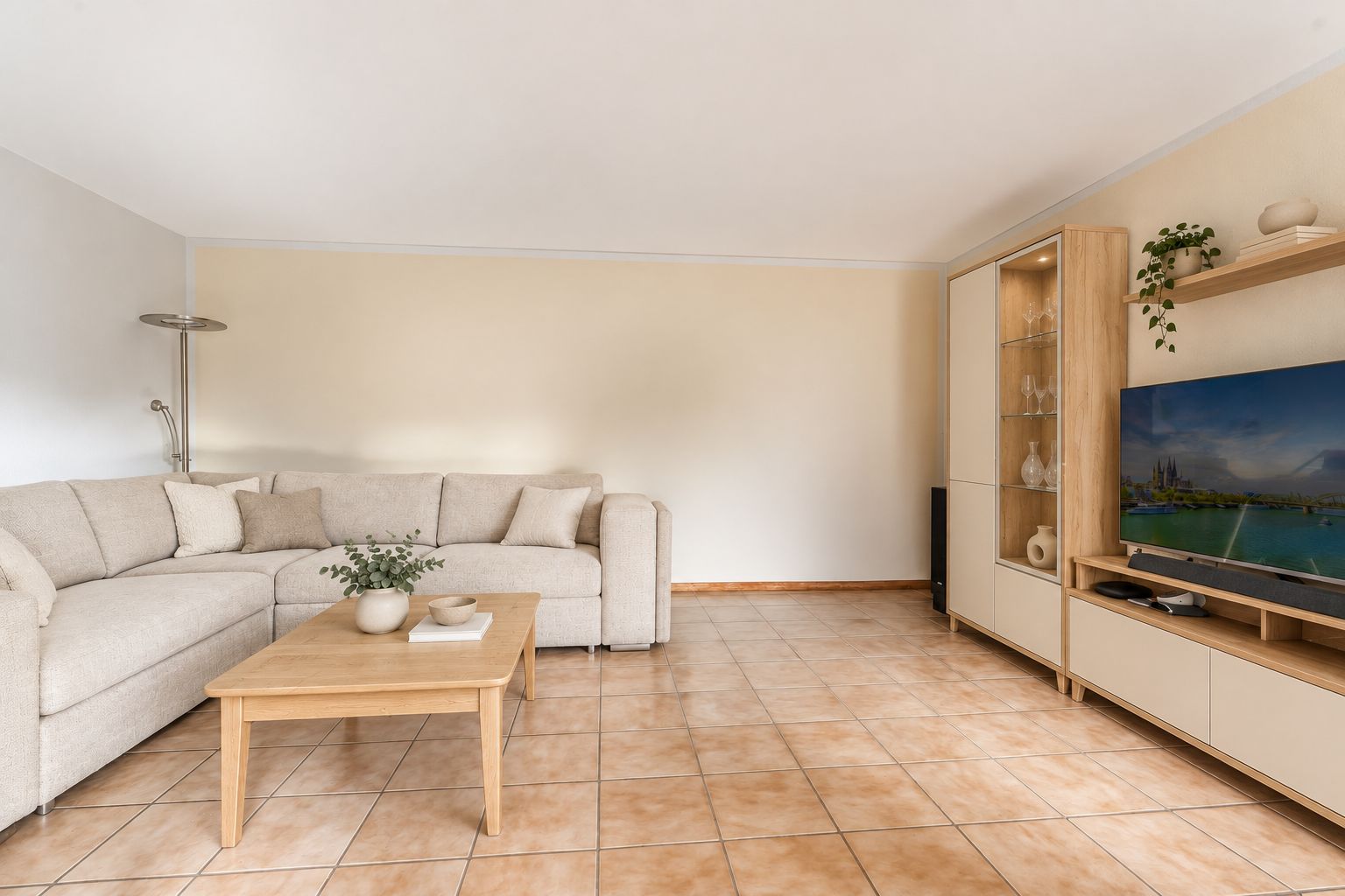Helles Wohnzimmer mit Ecksofa, Couchtisch, TV-Möbel und Fliesenboden.