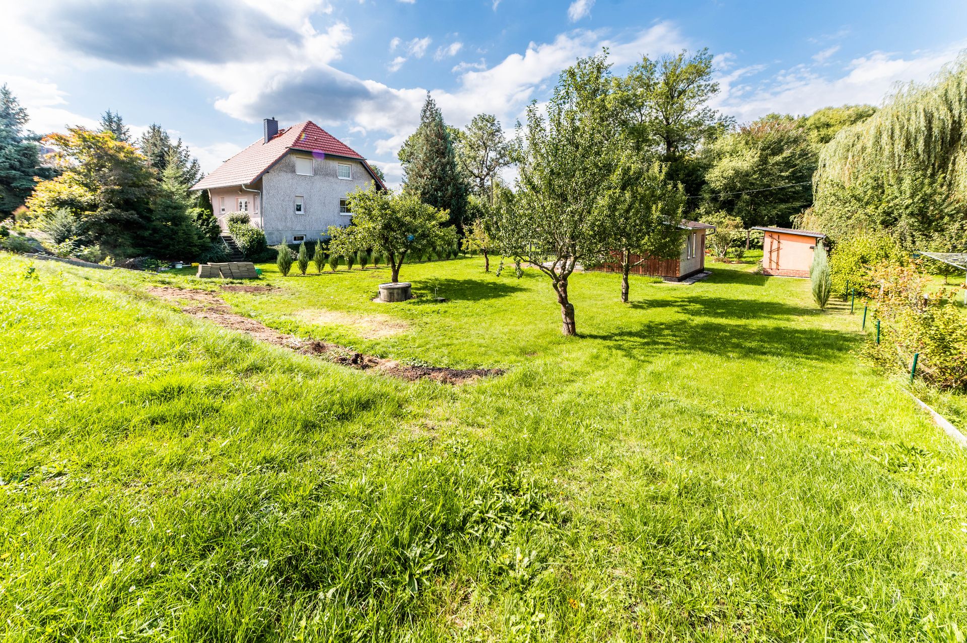 Großer grüner Garten mit Bäumen, Rasen und einem Wohnhaus im Hintergrund.