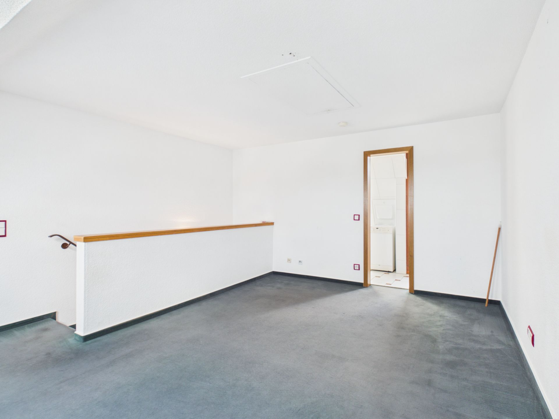 Leerer, heller Raum mit Teppichboden, offenem Geländer und einer Tür zu einem anderen Zimmer.