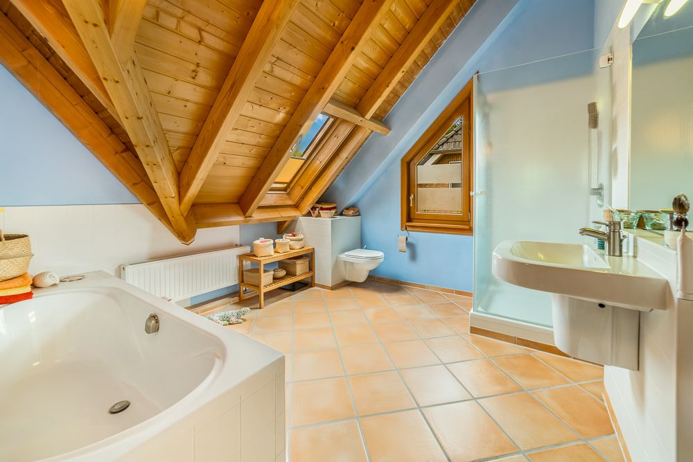 Modernes Badezimmer mit Badewanne, Dusche, Waschbecken und Dachschräge aus Holz.