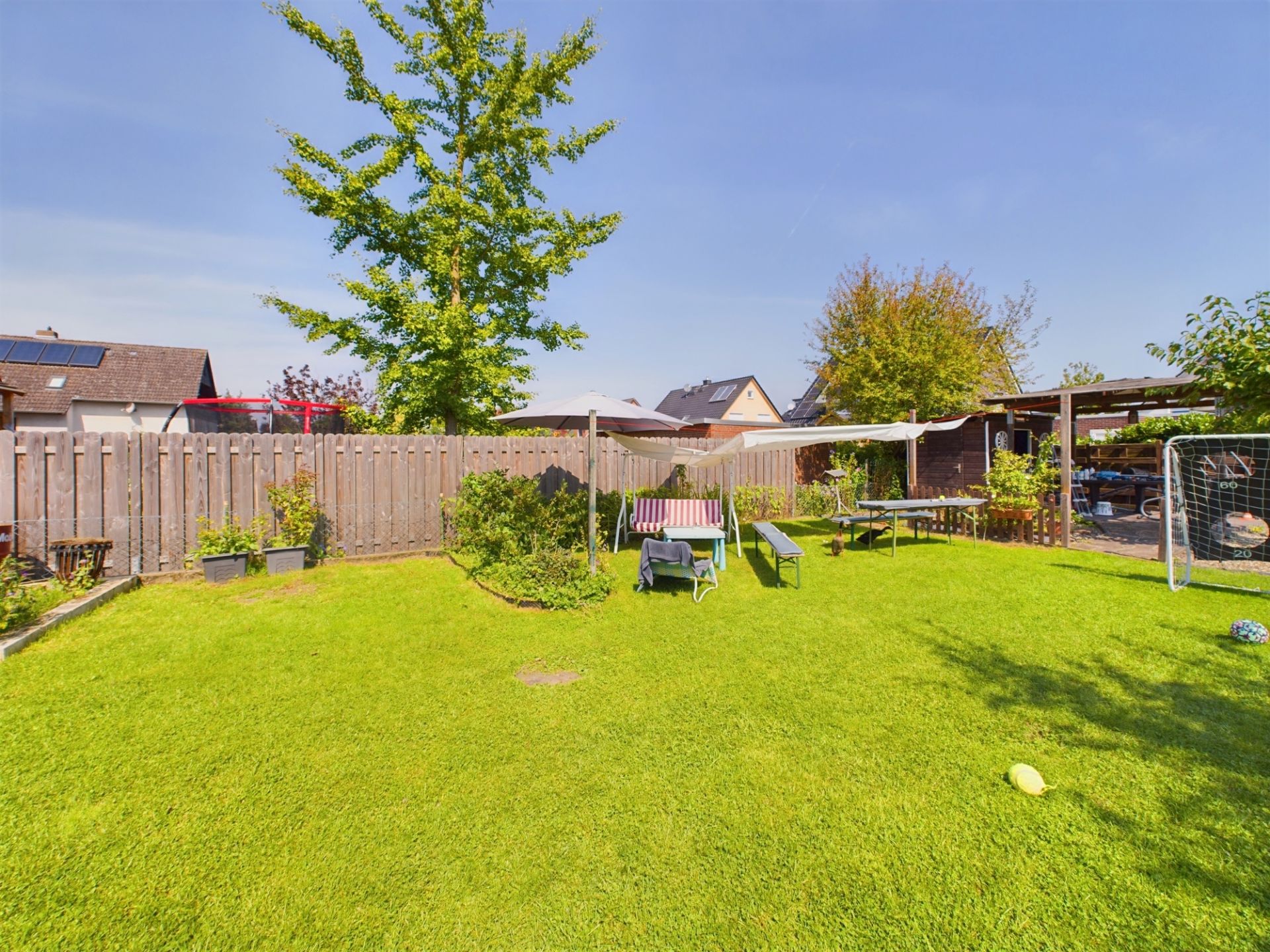 Grüner Garten mit Liegen, Tisch, kleiner Torwand und Holzzaun im Hintergrund.