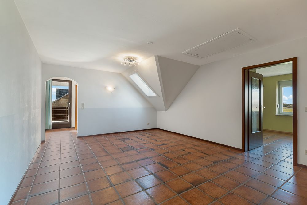 Leerer Raum mit braunen Fliesen, Dachfenster und zwei Türen, eine führt auf einen Balkon.