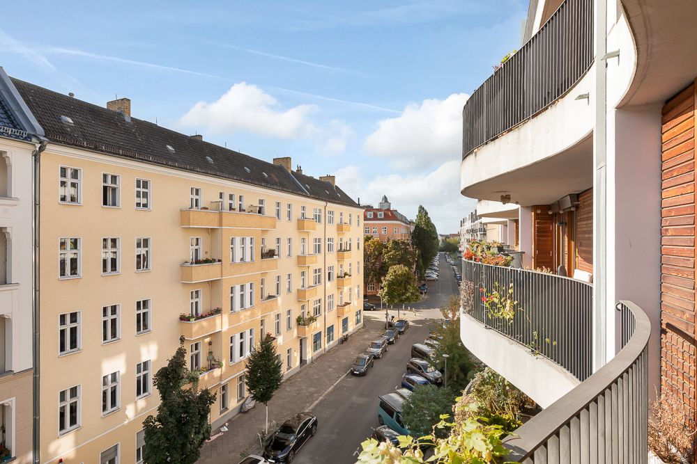Blick von einem Balkon auf eine ruhige Straße mit Wohnhäusern und geparkten Autos.