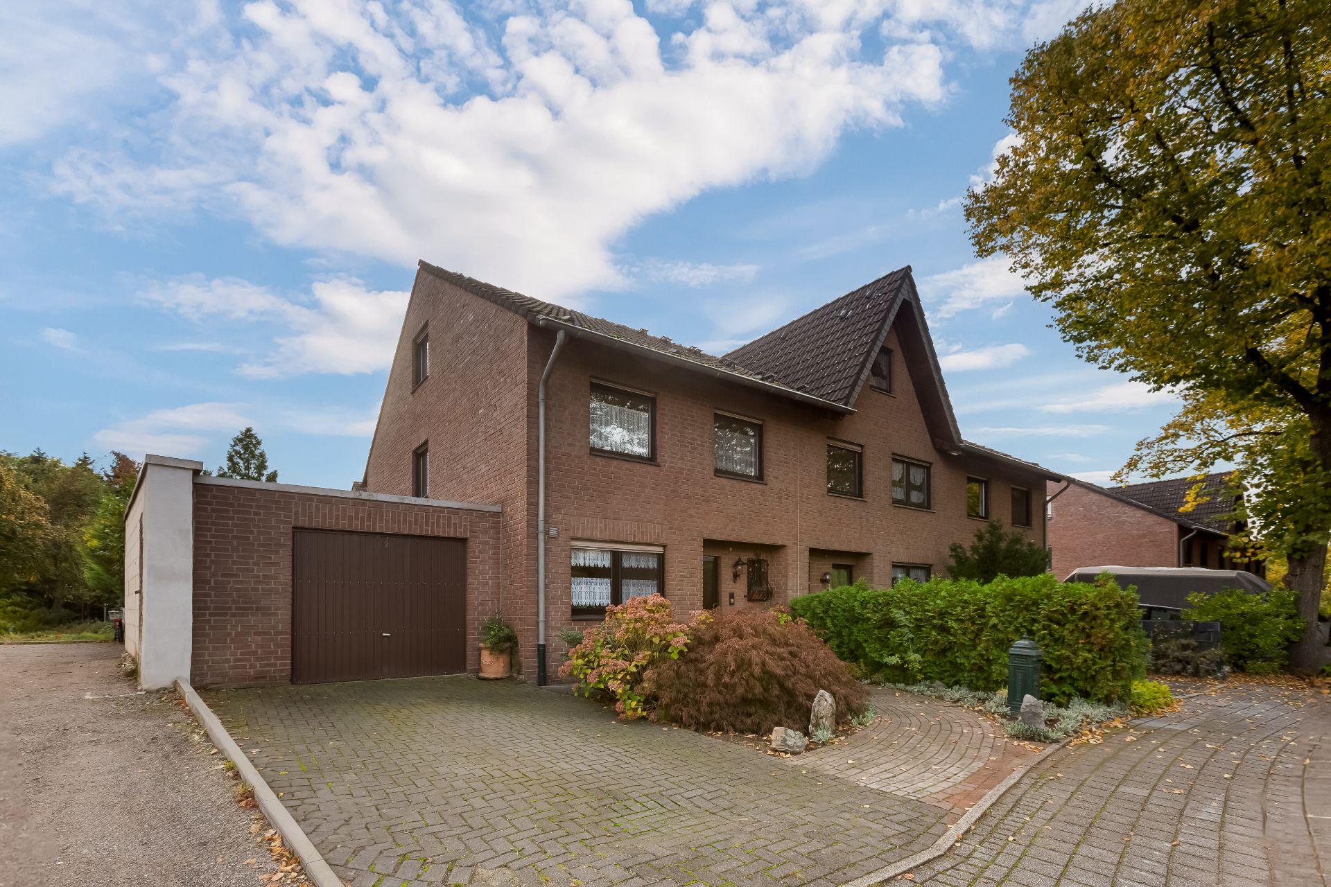 Zweistöckiges Backsteinwohnhaus mit Garage, gepflasterter Einfahrt und viel Grün im Vorgarten.