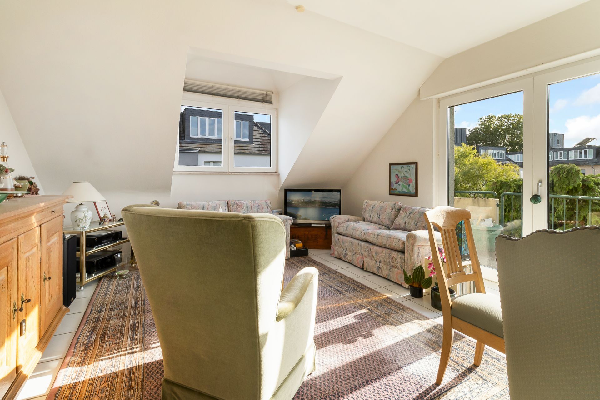 Helles Wohnzimmer mit Sofa, Sessel, Teppich und Balkonzugang.
