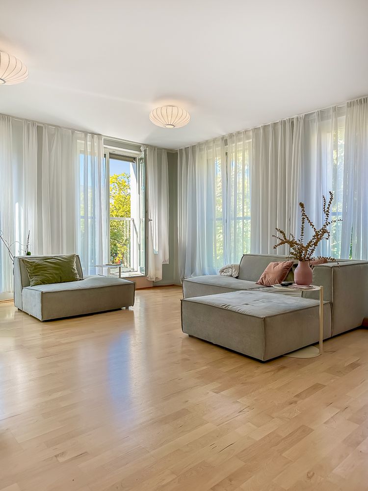 Helles Wohnzimmer mit großen Fenstern, Vorhängen, zwei Sofas und Holzboden.