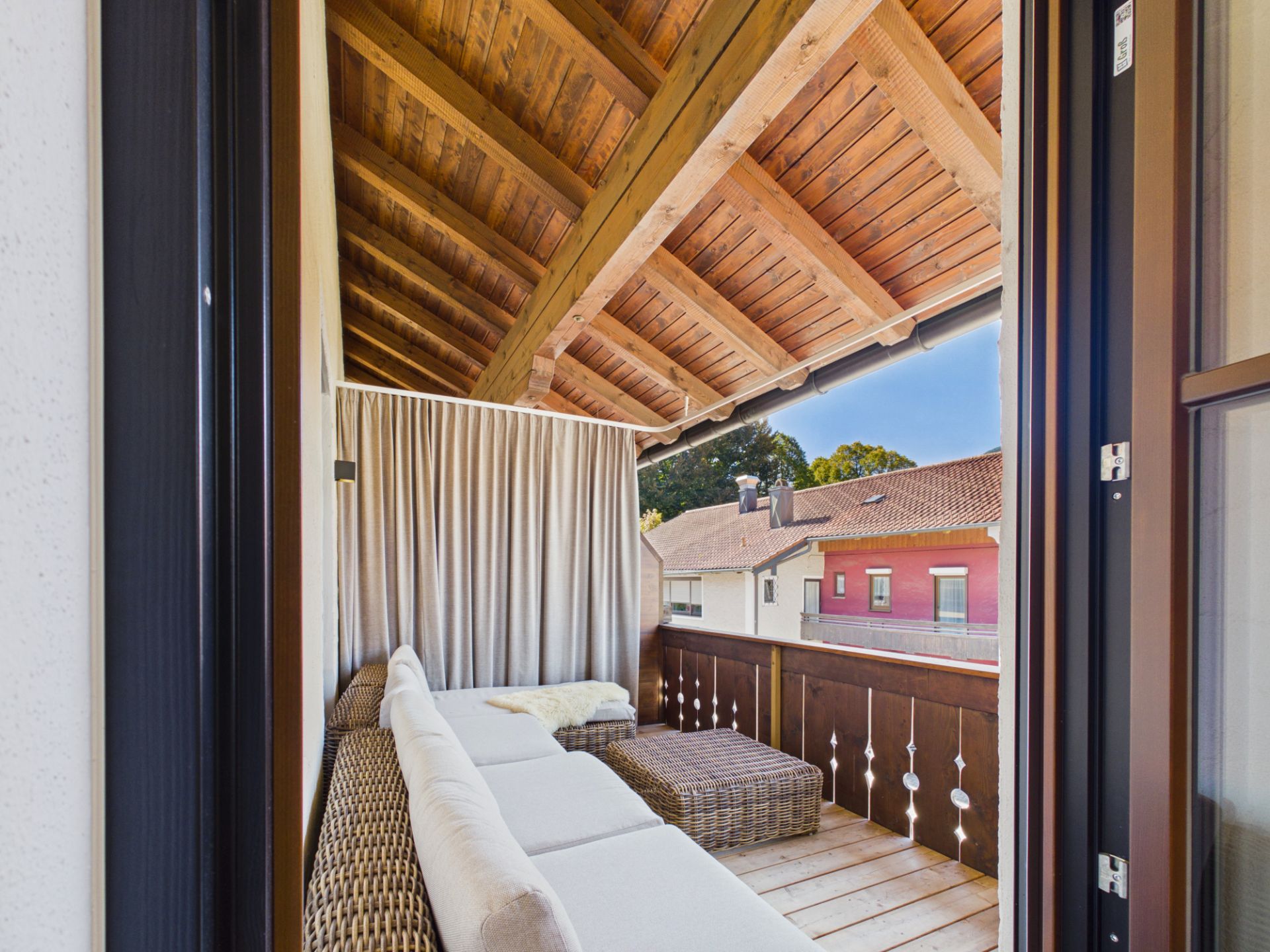 Überdachter Balkon mit Sofa, Couchtisch und Vorhang, Blick auf Nachbarhäuser.