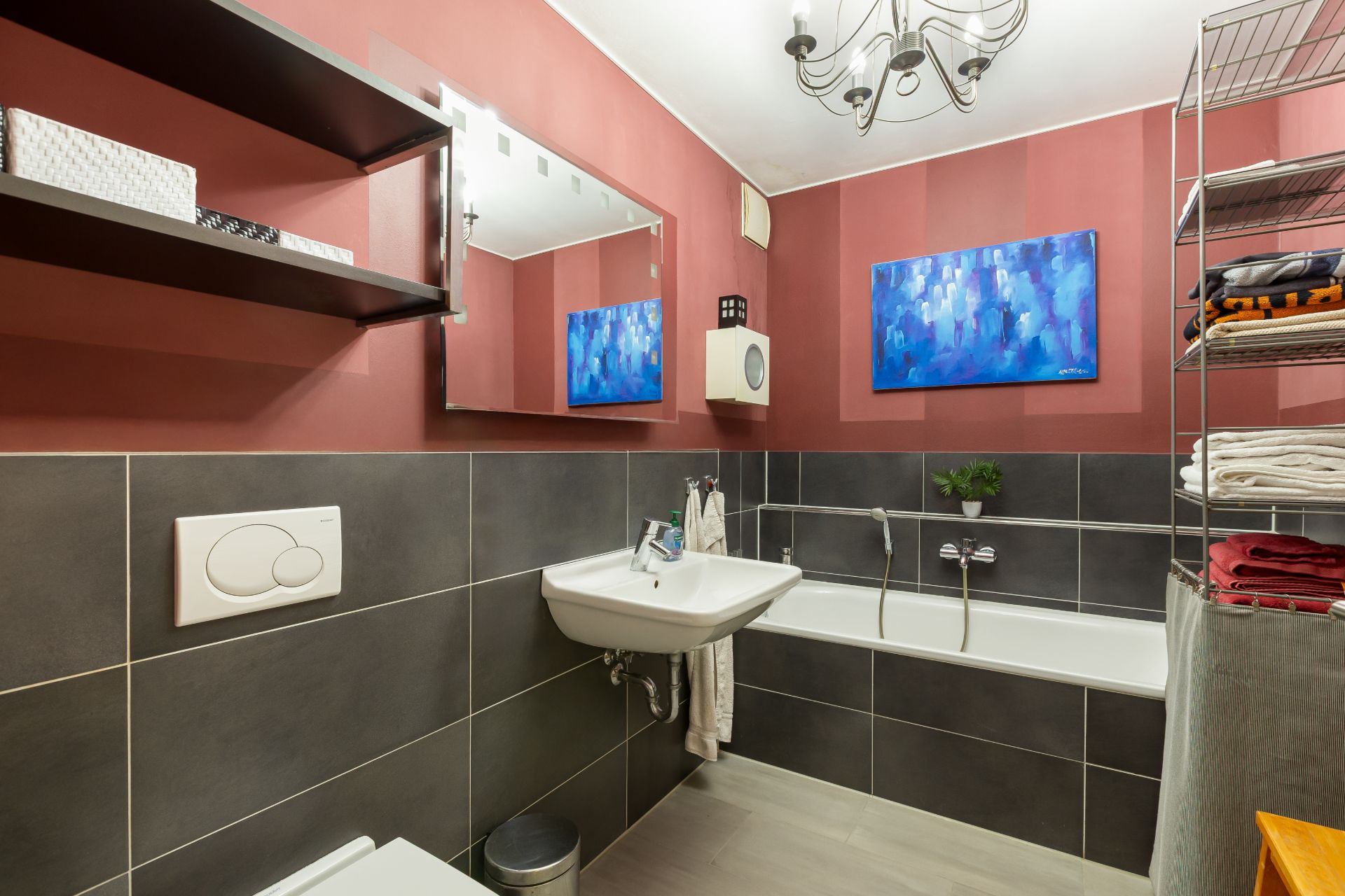Modernes Badezimmer mit roter Wand, Spiegel, Waschbecken, Badewanne und Regal mit Handtüchern.