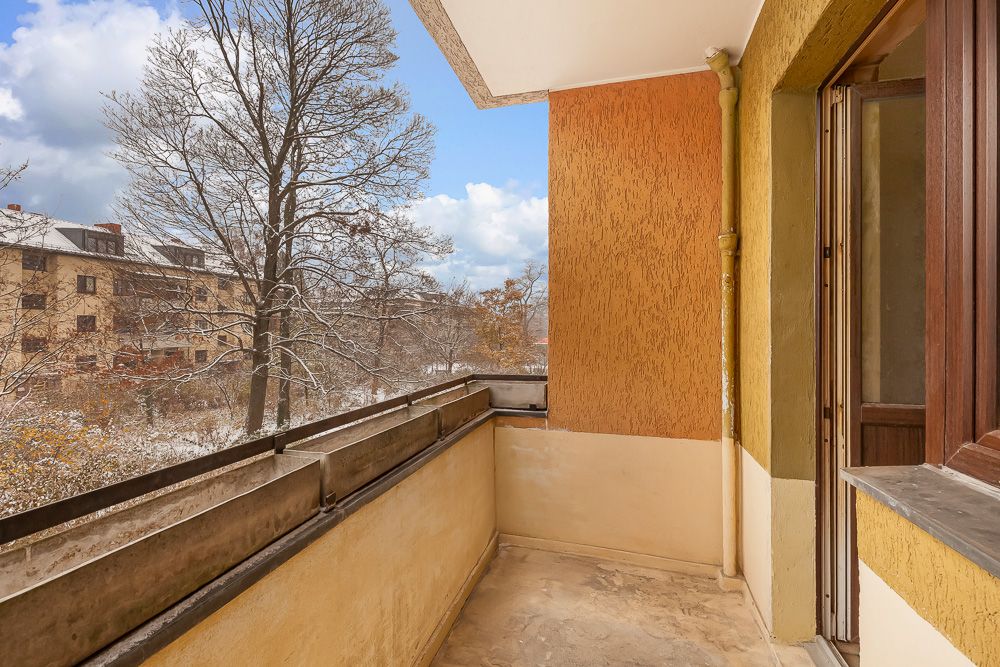 Balkon mit gelber Wandfarbe, Ausblick auf verschneite Bäume und benachbarte Häuser.