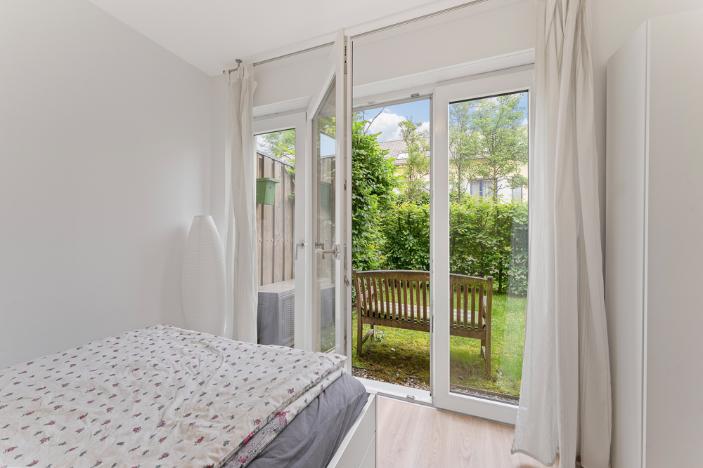 Schlafzimmer mit offenem Glasdoppeltür, Blick auf Garten und Holzbank.