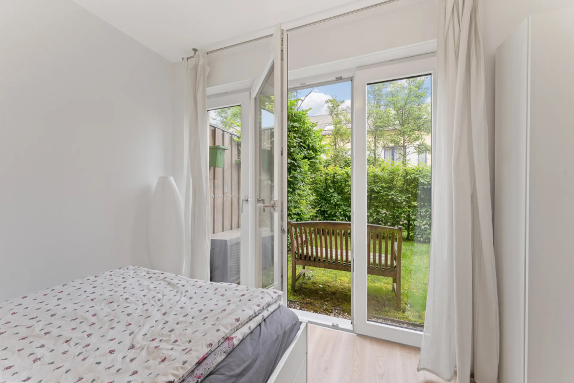 Schlafzimmer mit offenem Glasdoppeltür, Blick auf Garten und Holzbank.