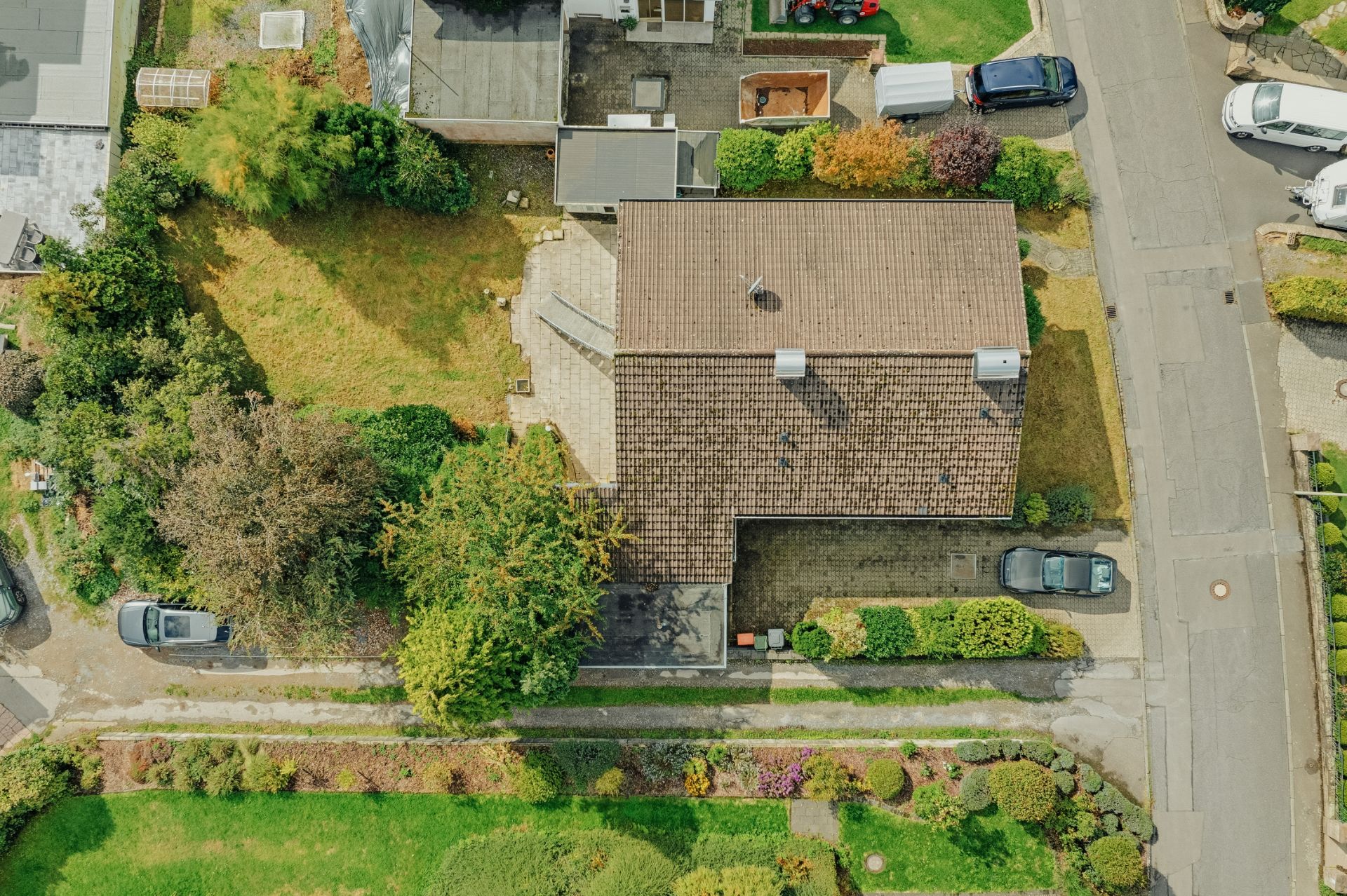 Luftaufnahme eines Wohnhauses mit Garten, Einfahrt und parkenden Autos in einer Wohnstraße.