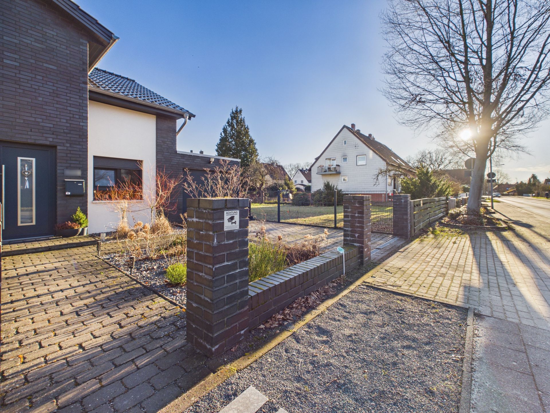 Vorgarten eines modernen Wohnhauses mit gepflastertem Weg und dunklem Zaun.