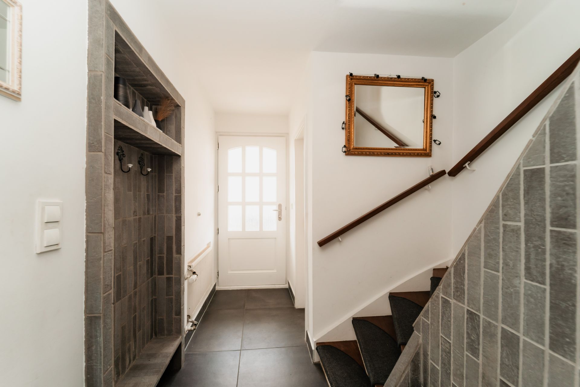 Heller Flur mit Fliesenboden, Treppe, Garderobe und Wandspiegel.
