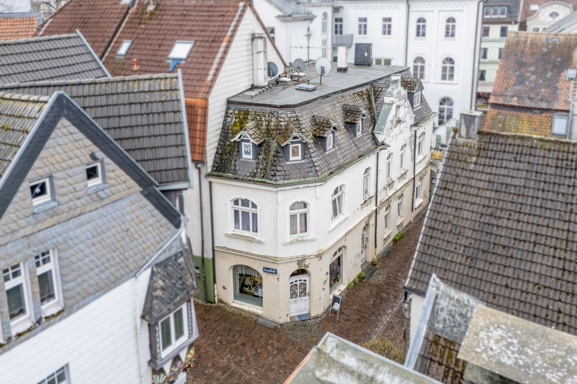 Mehrstöckiges Wohnhaus mit Schaufenstern unten und Ziegeldach in einer engen Gasse.