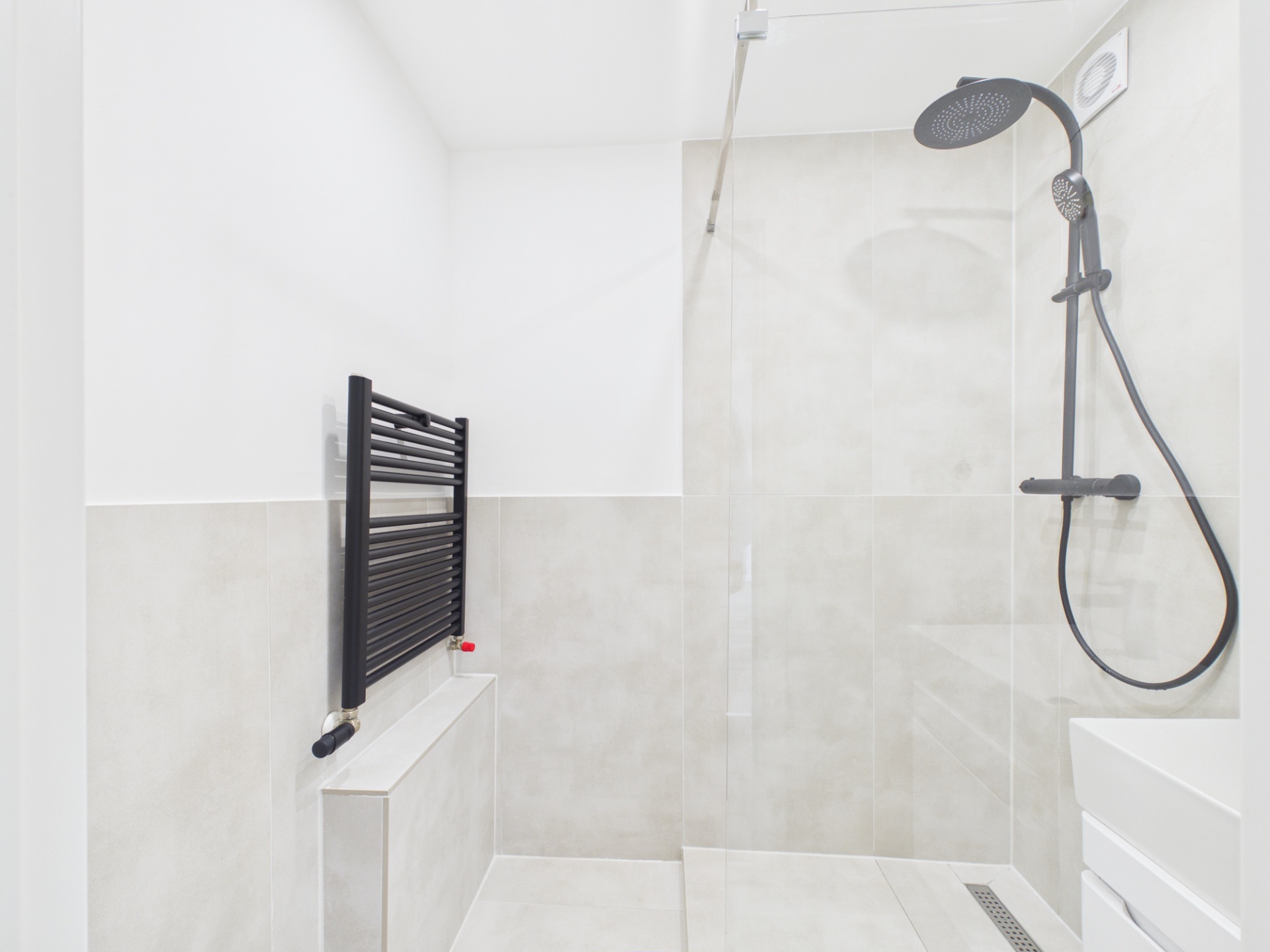 Helles Badezimmer mit großer Dusche, schwarzer Regenbrause und schwarzem Handtuchheizkörper.