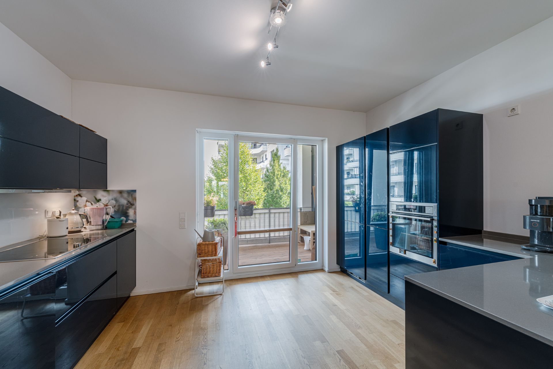Moderne Küche mit Holzfußboden, schwarzen Schränken und Zugang zu einem Balkon mit Pflanzen.