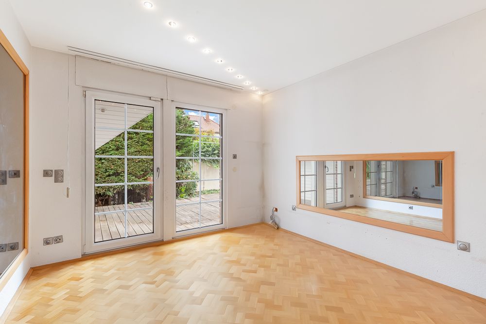 Heller Raum mit Parkettboden, großem Spiegel an der Wand und Glastüren zur Terrasse.