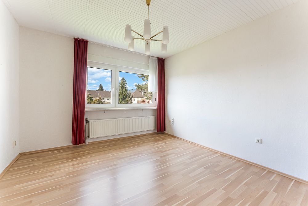 Leeres Zimmer mit Holzfußboden, weißer Decke, großes Fenster und roten Vorhängen.