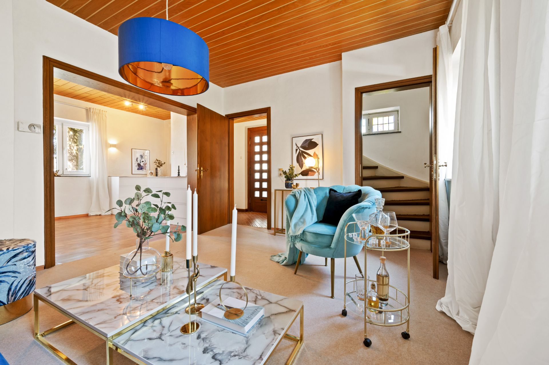Modernes Wohnzimmer mit Marmor-Couchtisch, blauem Sessel und Barwagen, offene Türen zu Flur und Treppe.