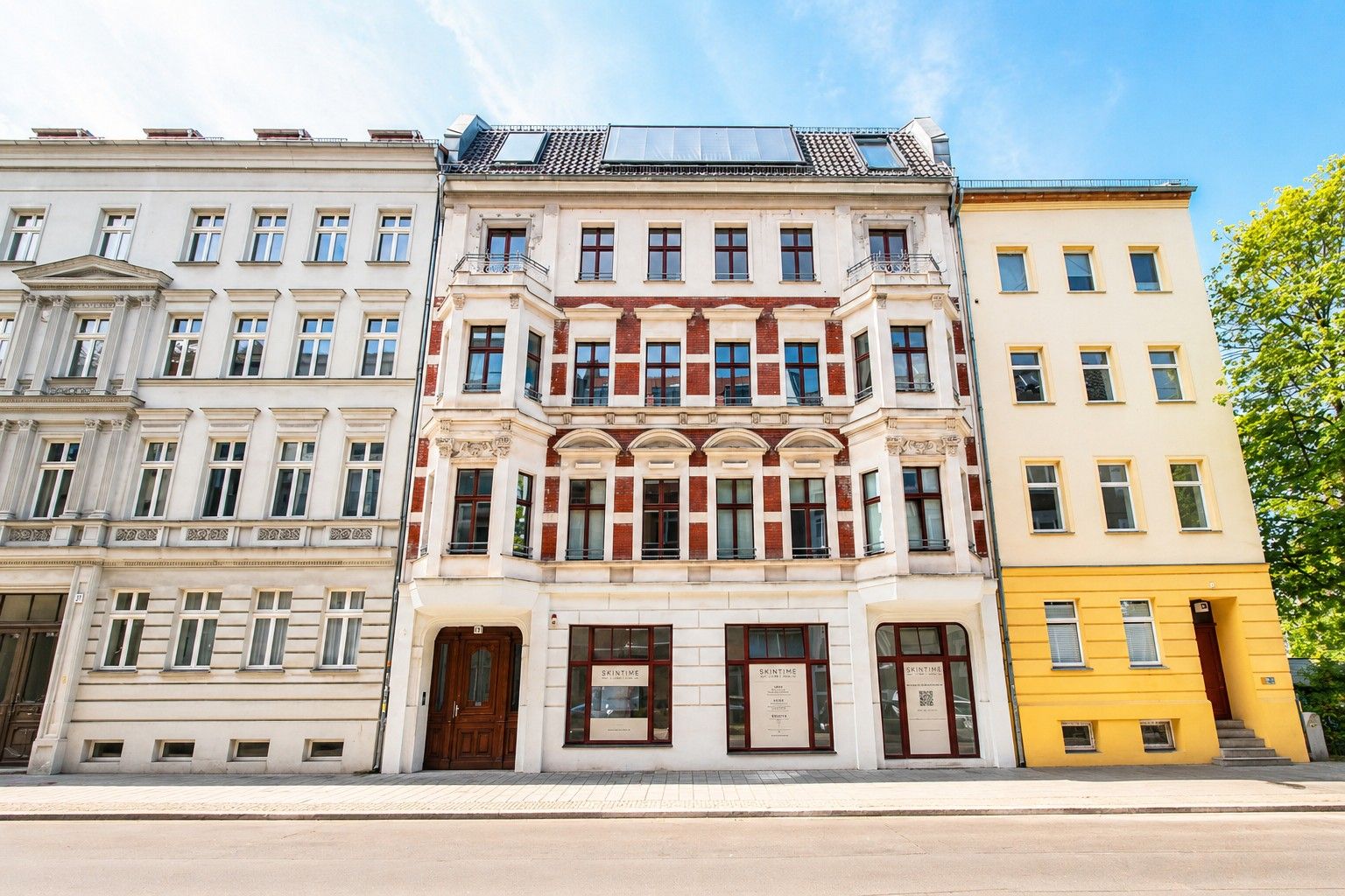 Mehrstöckiges Wohnhaus mit roter und weißer Fassade, großen Fenstern und Holztür.
