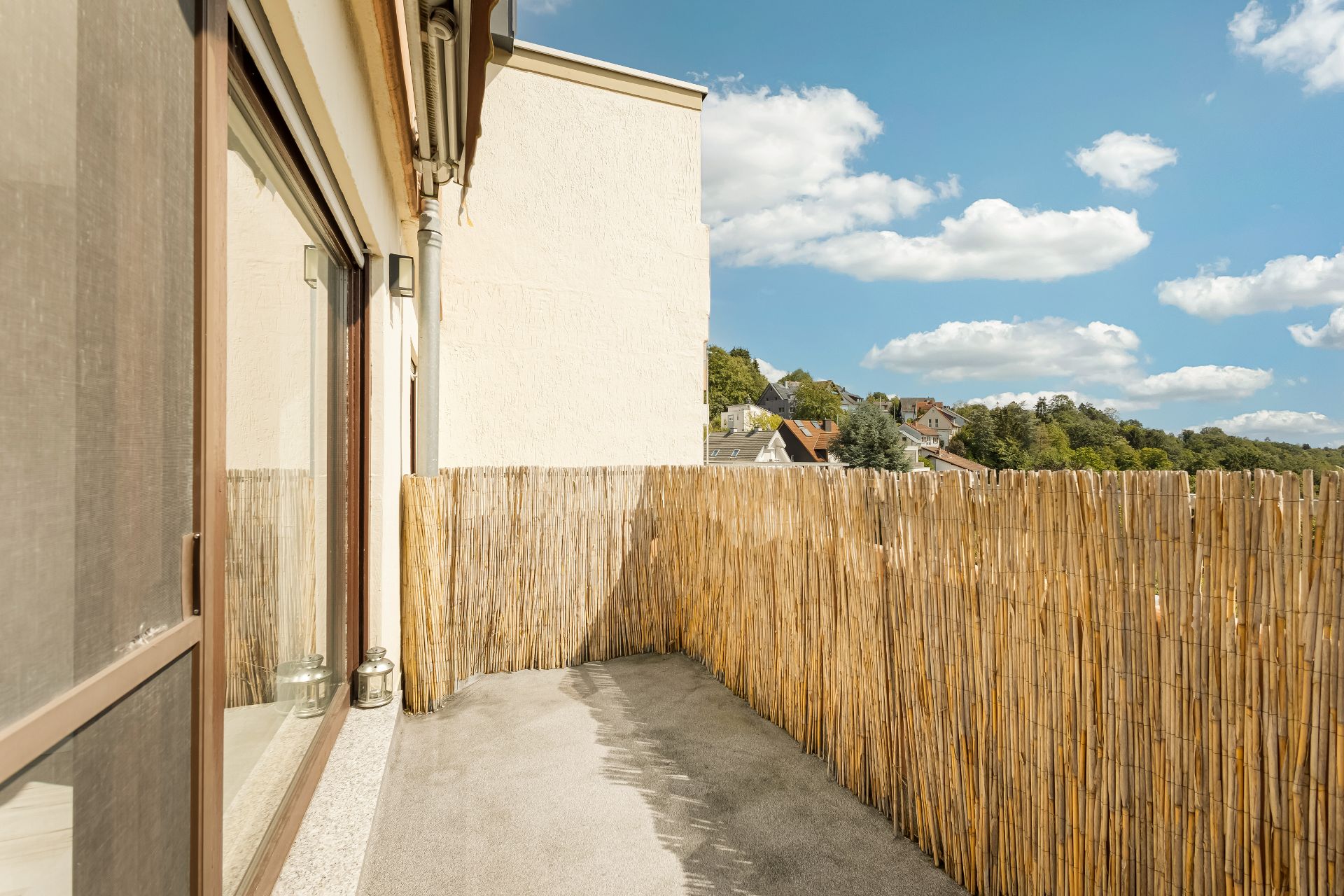 Balkon mit Sichtschutz aus Bambus und Blick auf Nachbarhäuser und blauen Himmel.