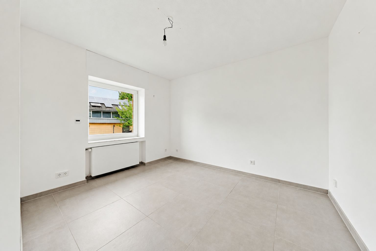 Leerer, heller Raum mit Fliesenboden und großem Fenster, weiße Wände und Decke.