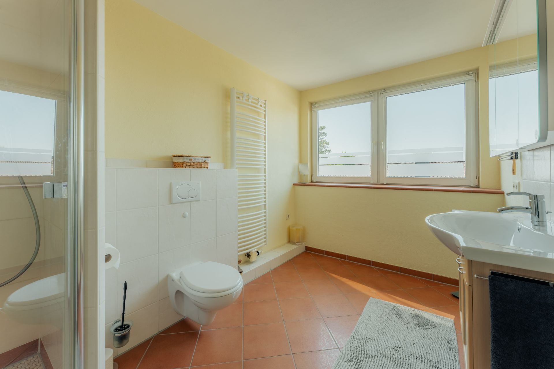 Helles Badezimmer mit Dusche, WC, Waschbecken und großem Fenster.