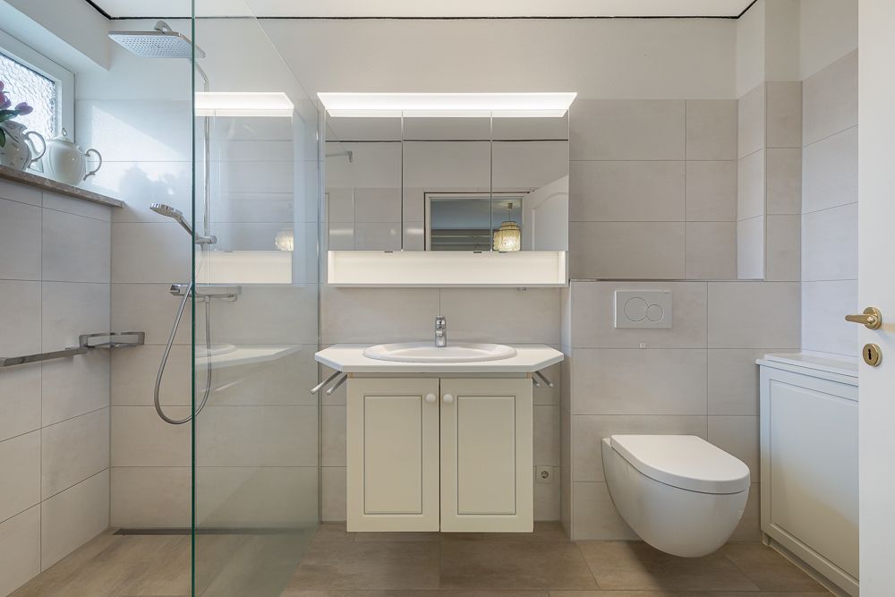 Modernes Badezimmer mit großer Dusche, Waschbecken, Spiegel und wandhängender Toilette.