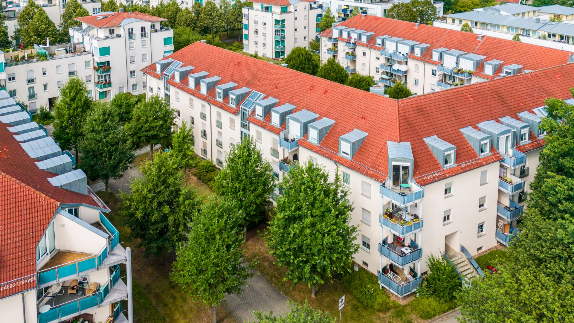 Mehrere Wohngebäude mit roten Dächern und Balkonen, von Bäumen umgeben.