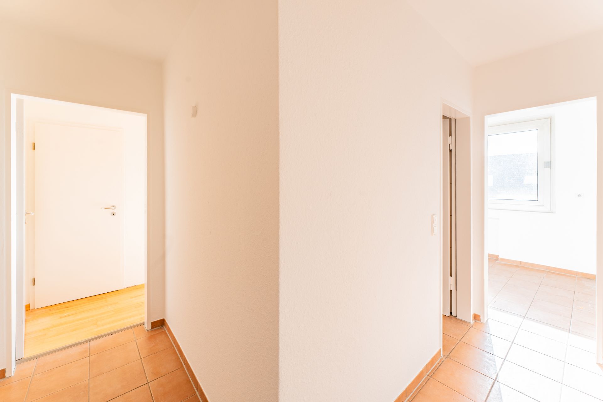 Heller Flur mit Fliesenboden, mehreren Türen und einem Fenster im Hintergrund.