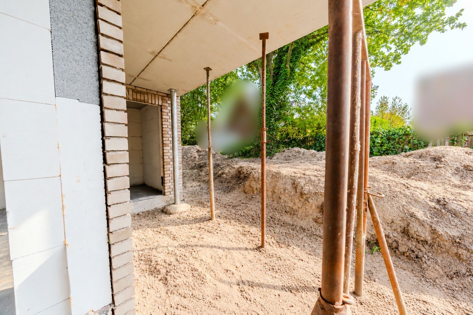 Baustelle mit unverputzten Wänden, Stützen und Sandboden im Außenbereich eines Hauses.