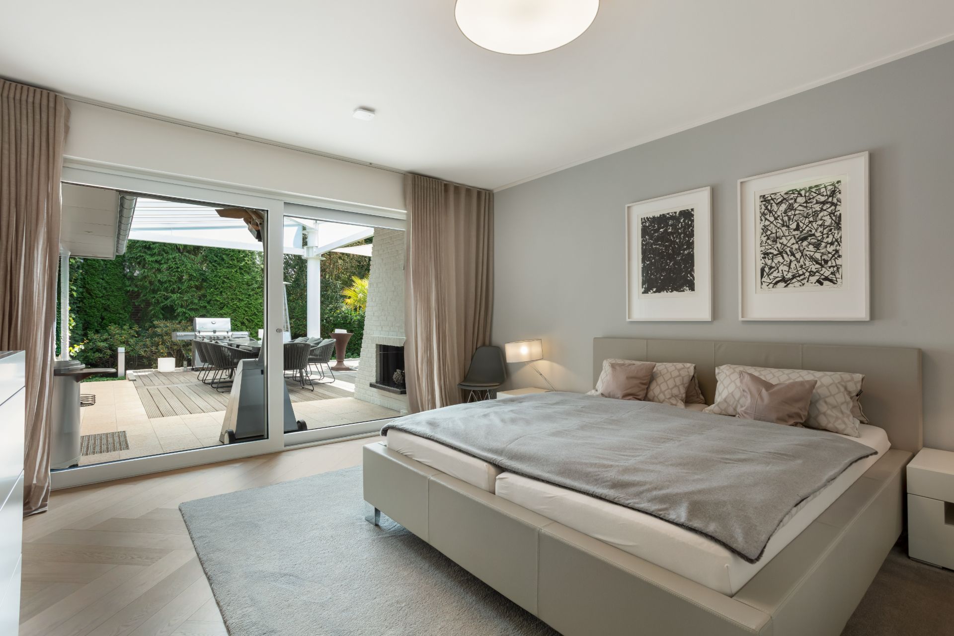 Modernes Schlafzimmer mit großem Bett, Teppich und Zugang zur Terrasse mit Sitzbereich.