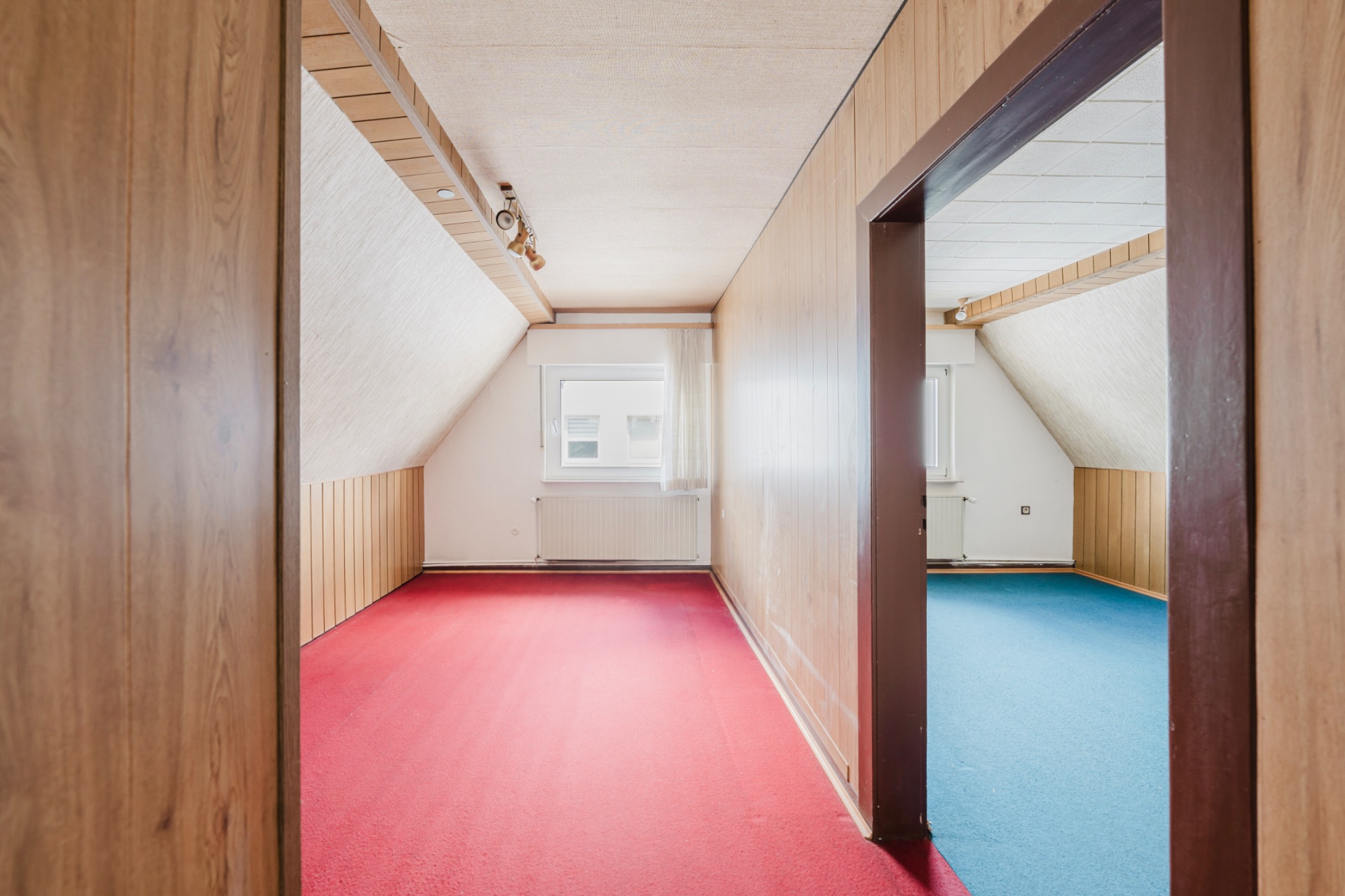 Zwei Dachzimmer mit Holzverkleidung, rotem und blauem Teppich, jeweils mit Fenster.