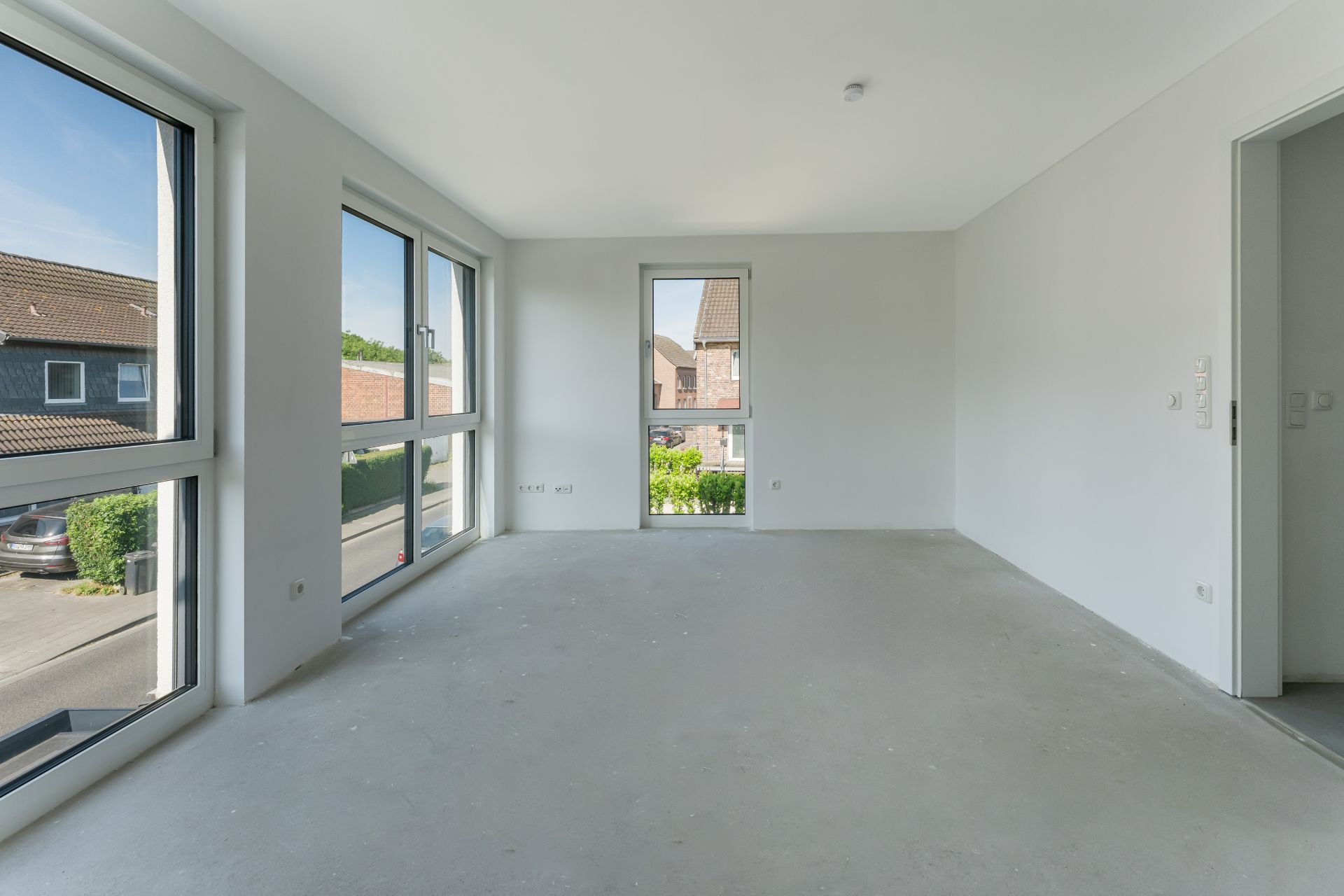 Leerer, heller Raum mit großen Fenstern und Blick auf eine Wohnstraße.