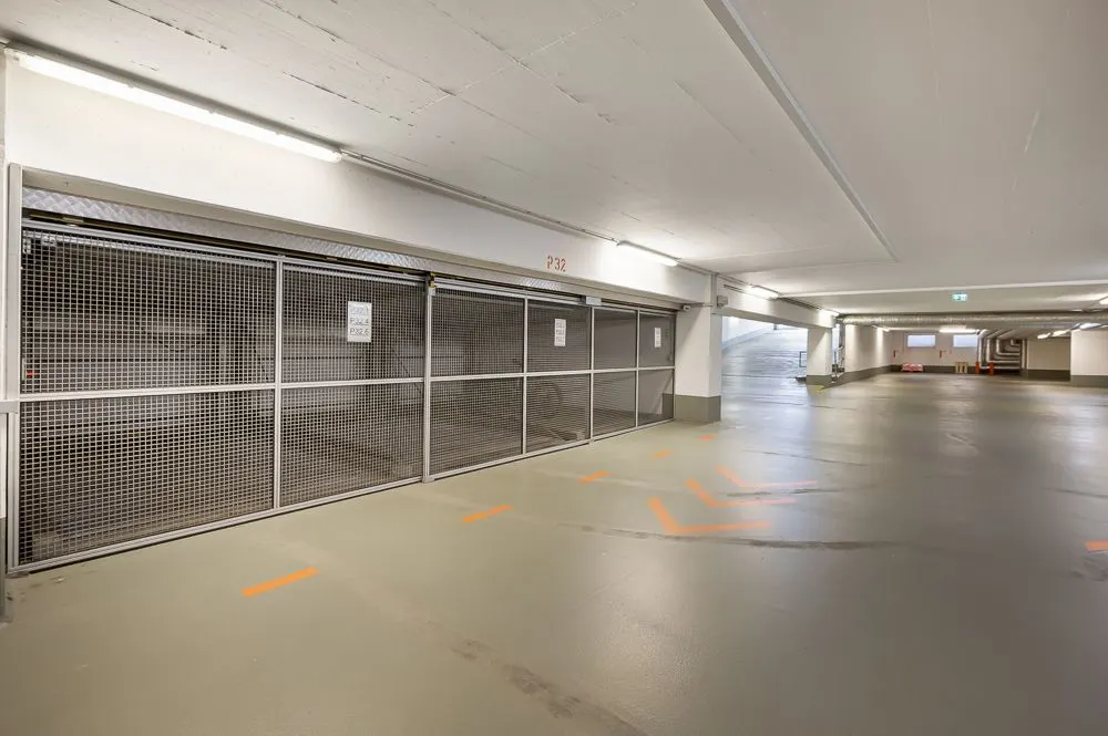 Leere Tiefgarage mit beleuchtetem, sauberem Boden und Gitterabtrennungen an den Parkplätzen.