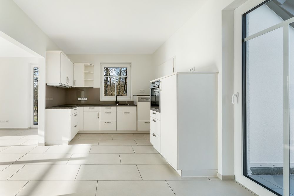 Helle Einbauküche mit weißen Schränken, Fenster und Zugang zur Terrasse.
