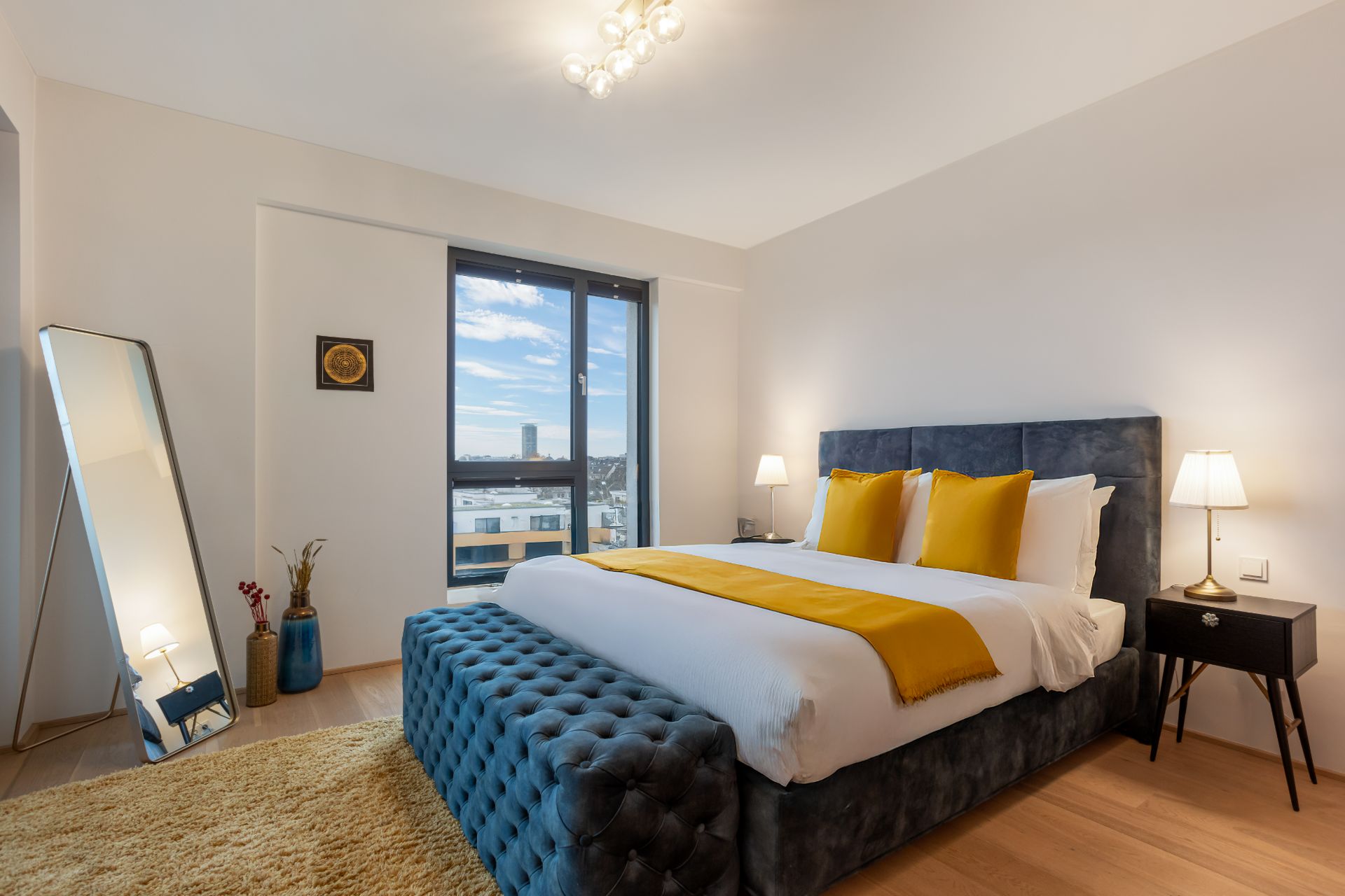 Modernes Schlafzimmer mit großem Bett, gelben Akzenten und bodentiefem Fenster.