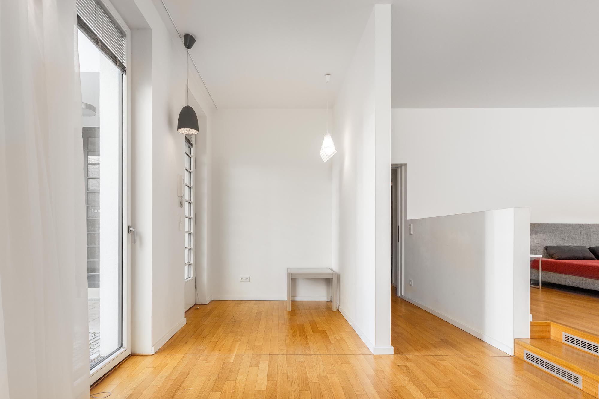 Heller Flur mit Holzboden, weißen Wänden, Hängelampen und einer Glastür.