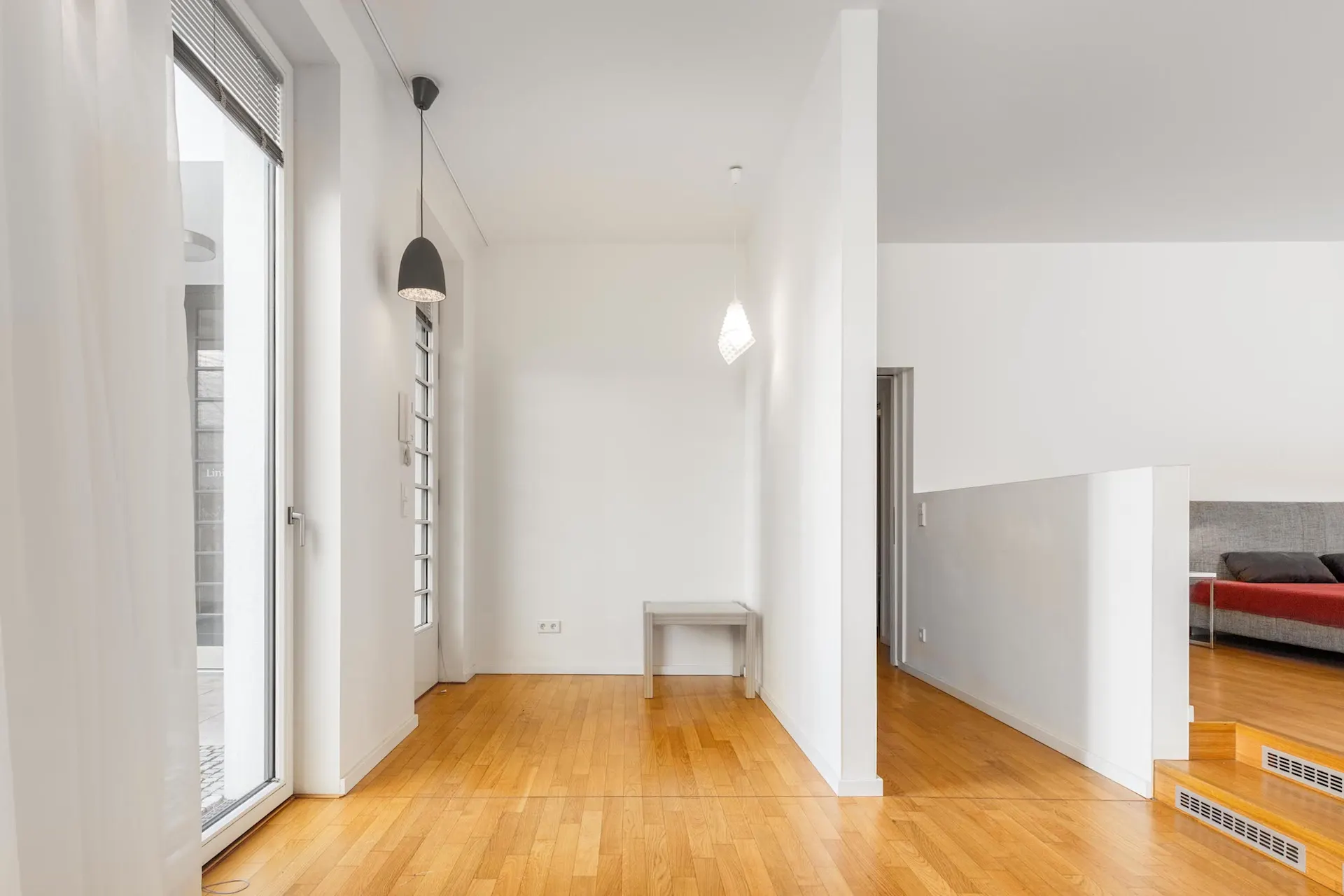 Heller Flur mit Holzboden, weißen Wänden, Hängelampen und einer Glastür.