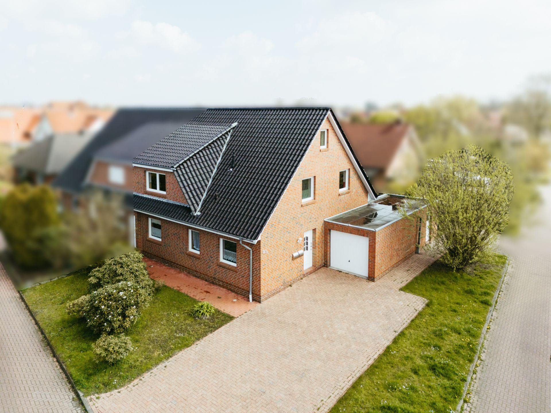 Backstein-Einfamilienhaus mit schwarzem Dach, Garage und gepflasterter Einfahrt.