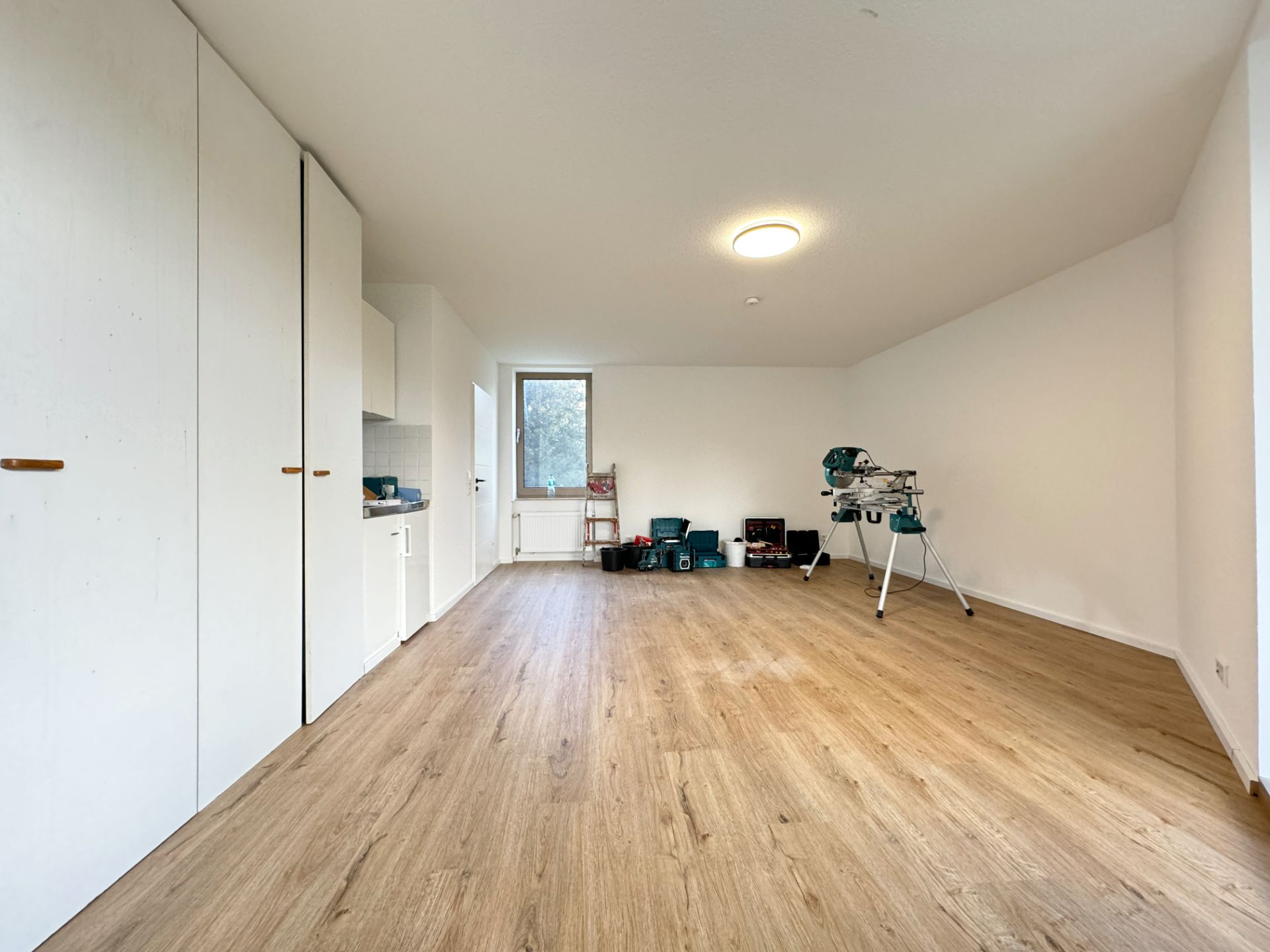 Heller Raum mit Holzboden, Einbauschränken, Fenster und Werkzeugen an der Wand.