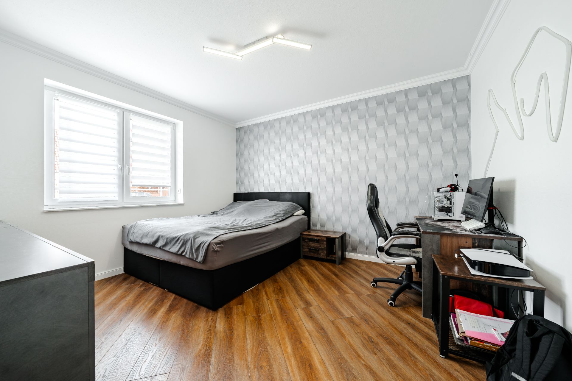 Schlafzimmer mit Doppelbett, Schreibtisch, Bürostuhl und großem Fenster, Holzboden.