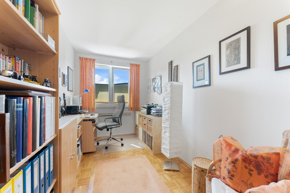 Helles Arbeitszimmer mit Schreibtisch, Regal, Stuhl, Sofa und Fenster mit Vorhängen.