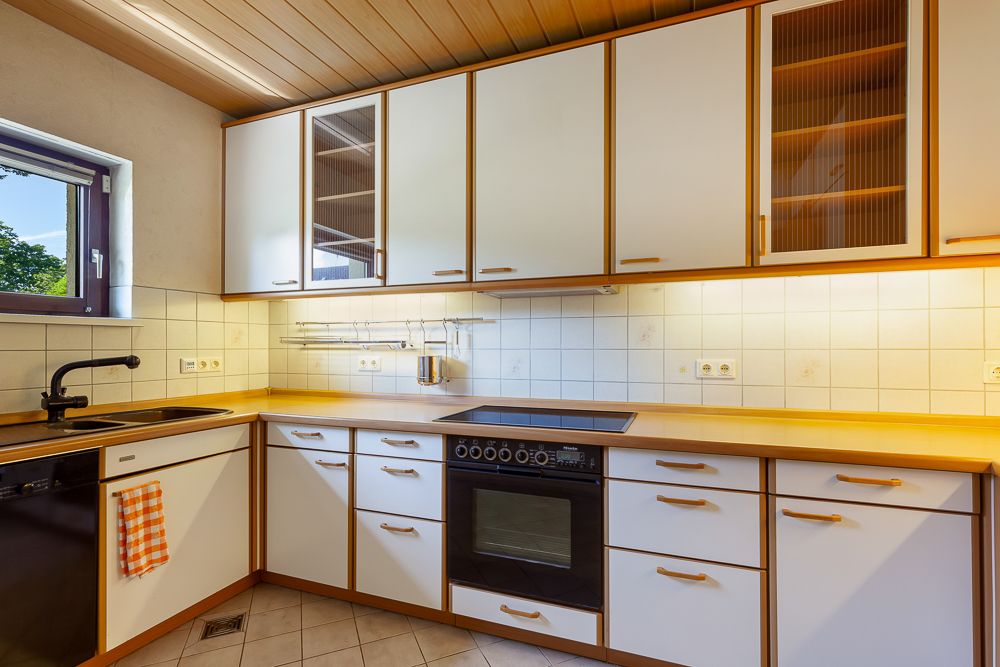Helle Einbauküche mit weißen Schränken, Herd, Spüle, Ofen und einem Fenster.